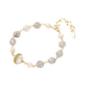 Bracelet with cloudy quartz beads, freshwater pearls, and gold-wrapped baroque pearl centerpiece on white background.