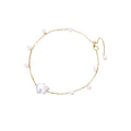 Delicate gold chain bracelet with baroque pearl centerpiece and small freshwater pearls on cream background.