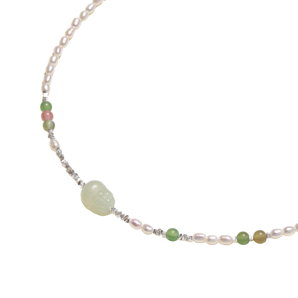 Delicate pearl necklace with pale green serpentine jade centerpiece and colorful agate beads on cream background