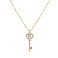 Delicate gold key pendant with heart-shaped bow and crystal pavé detailing on fine chain against cream background.