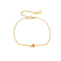Delicate gold chain bracelet with minimalist bar and centered knot detail on cream background